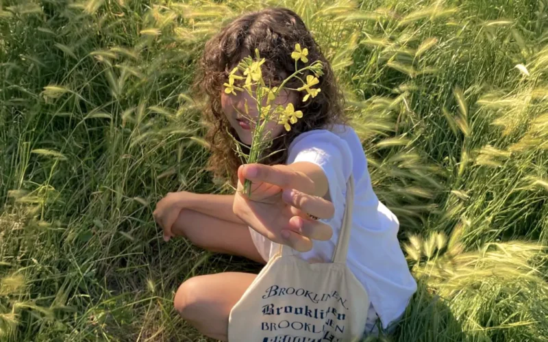 Young woman holding yellow flowers in a field, capturing a feminine and natural aesthetic, reflecting themes of femininity.